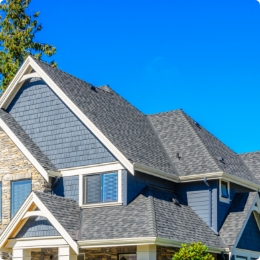 A large, elegant brick home with a gray shingle roof, multiple gables, and a small cupola on top.
